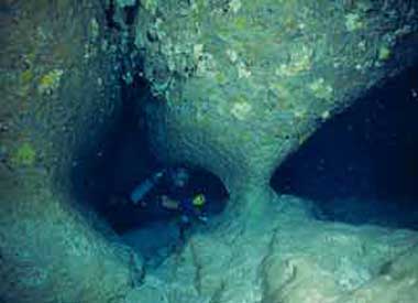 an image of a diver exploring the underwater cavern containing a stalagmite and stalactite which are so old they have joined together
