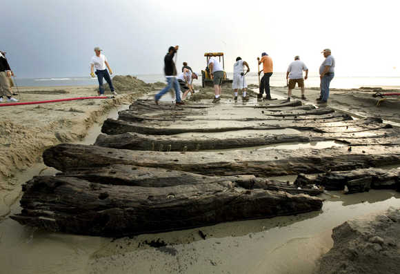 an image of a volunteers and members of the N.C. Wildlife Resources Commission working to remove what remains of a shipwreck on the beach in Corolla, which is also a clickable link direct to the News Observer story